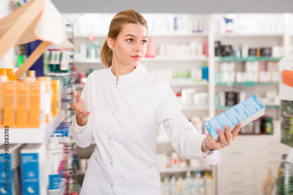 Smiling female pharmacist offering help in choosing at counter in pharmacy