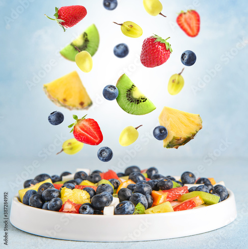 Fototapeta Naklejka Na Ścianę i Meble -  Plate with delicious fruit salad and flying ingredients on color background