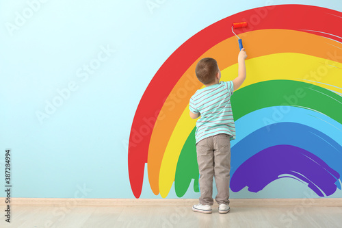 Cute little boy painting rainbow on blue wall