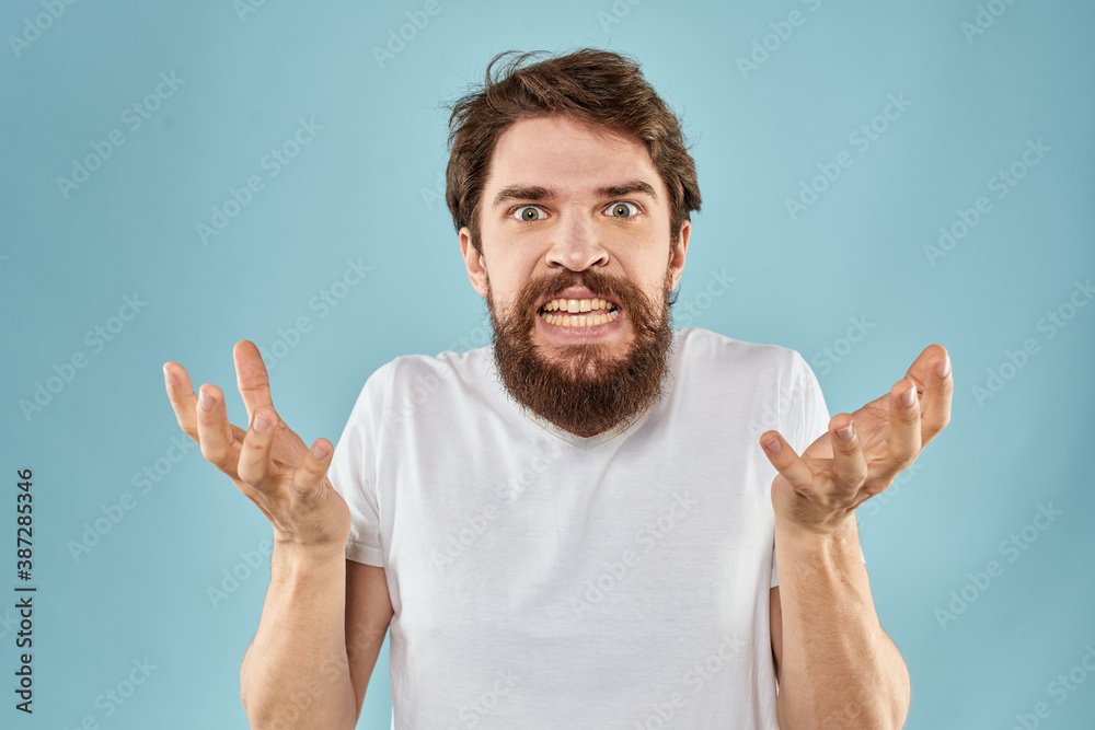Bearded man in white T-shirt emotions gestures with hands displeased facial expression blue background Bearded man in white T-shirt emotions gestures with hands displeased facial expression blue background