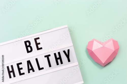 Lightbox with words Be Healthy and pink paper heart. Care of health and medical concept. World health day. photo