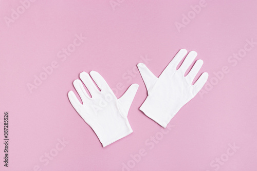 Pair of clothes gloves on pink paper background. Soft natural cotton fabric gloves white colored for cosmetic procedures. Wellness, healthcare and special clothes concept.