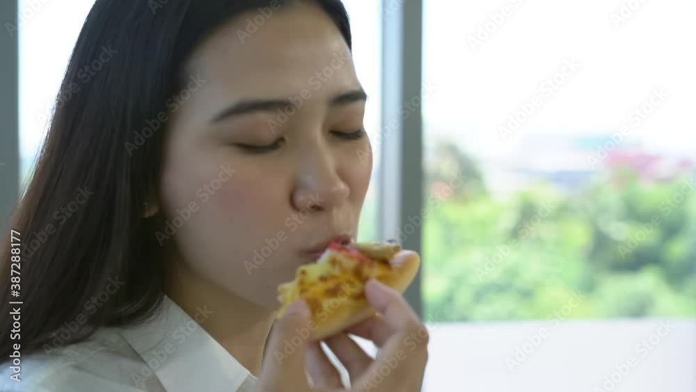 Asian young woman enjoy eating a piece of pizza in the office during a break. Asian young woman enjoy eating a piece of pizza in the office during a break.