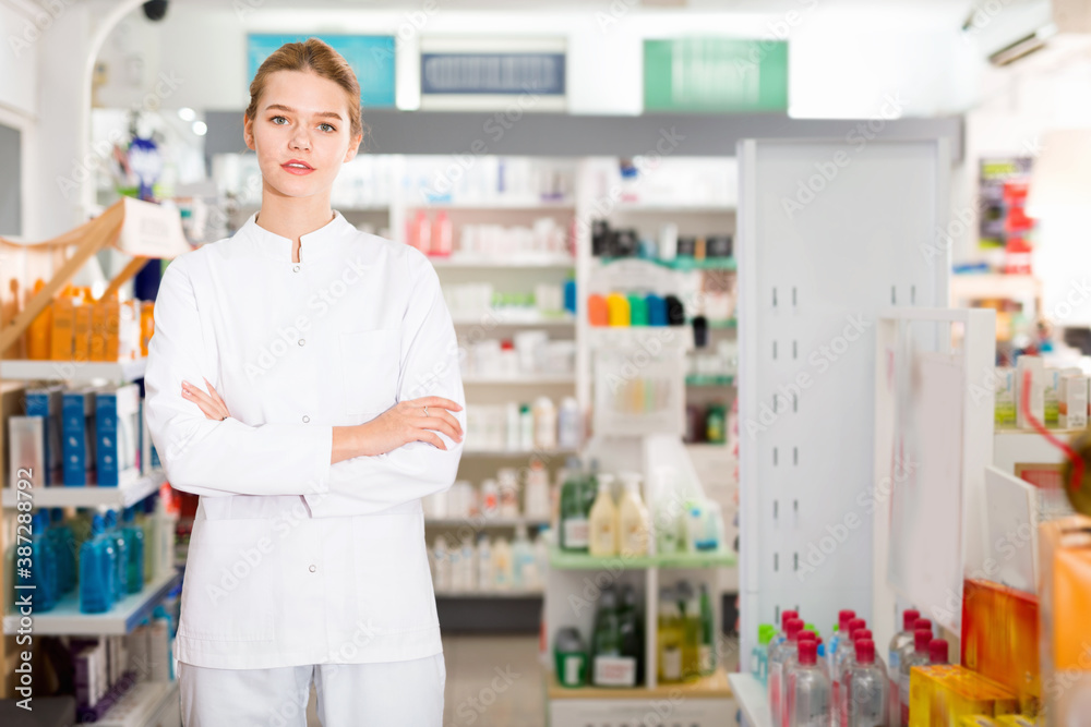 Portrait of young pleasant smiling positive female pharmacist in modern drugstore