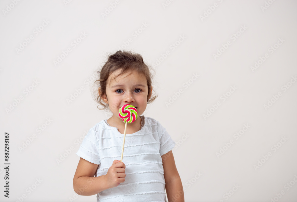 A small girl on a bright background stands with a lollipop in front of his face. Isolated. A small girl on a bright background stands with a lollipop in front of his face. Isolated.