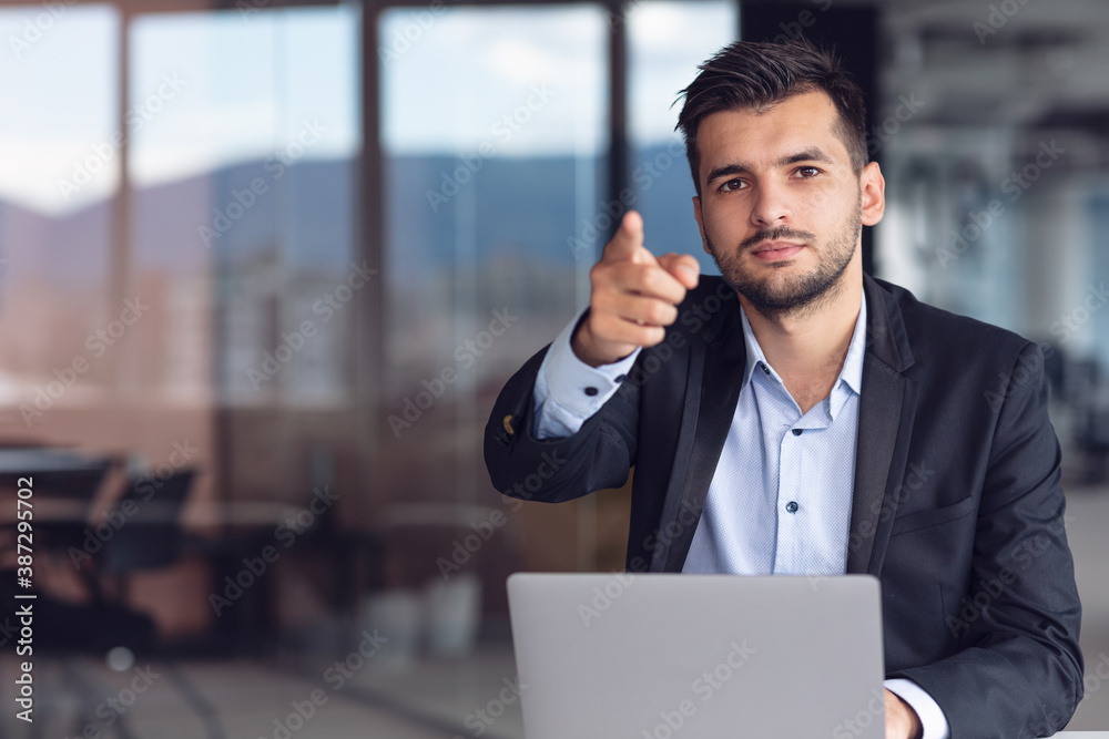 Man Sitting At Office Desk With Laptop Pointing Man Sitting At Office Desk With Laptop Pointing