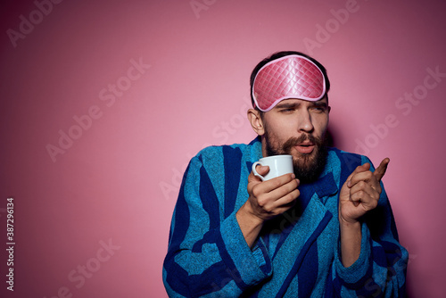 Man with a cup of tea in his hand and with a pink mask on his face on a pink background cropped view © SHOTPRIME STUDIO