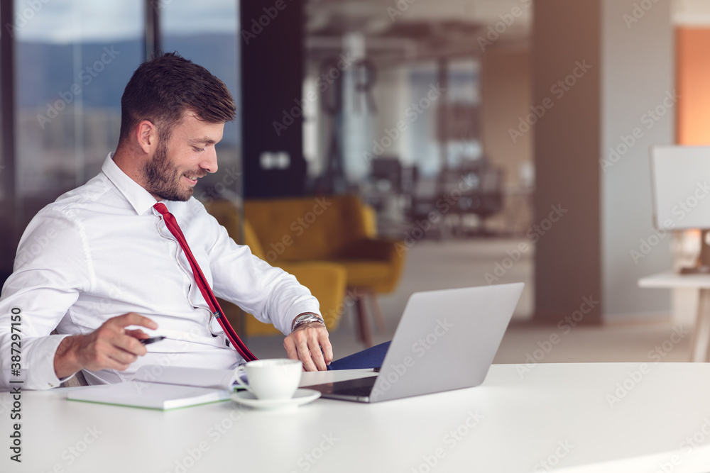 Casual Day In Office. Smiling Male Employee Using Laptop And Drinking Coffee.