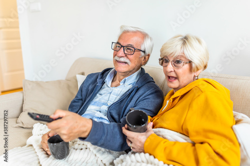Portrait of senior couple watching television at home, sitting on sofa, covered with blanket