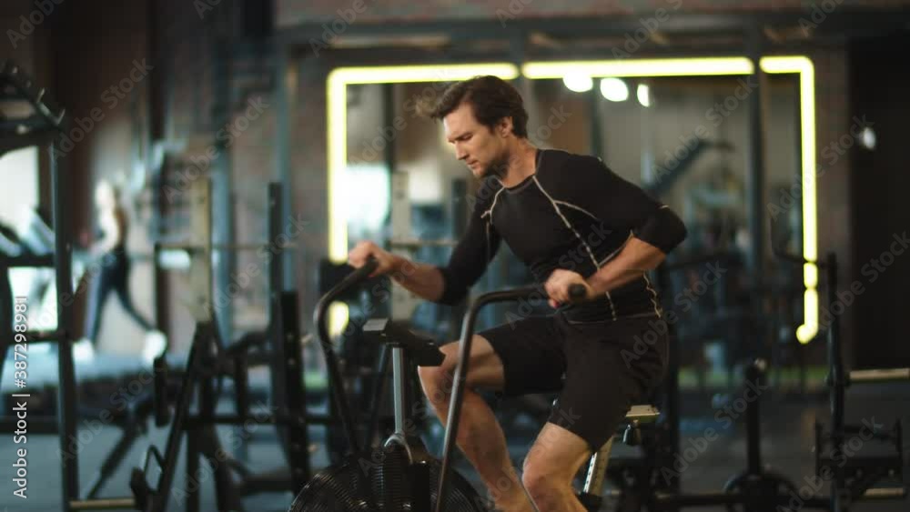 Eager athlete doing cardio in sport club. Fit man training on exercycle at gym