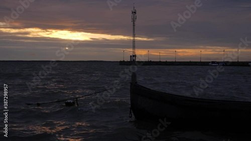 Old wooden fishing boat during small waves in the Kuršių Marios, Lithuania, during beautiful sunrise. The silhouette of communication tower in the distance photo