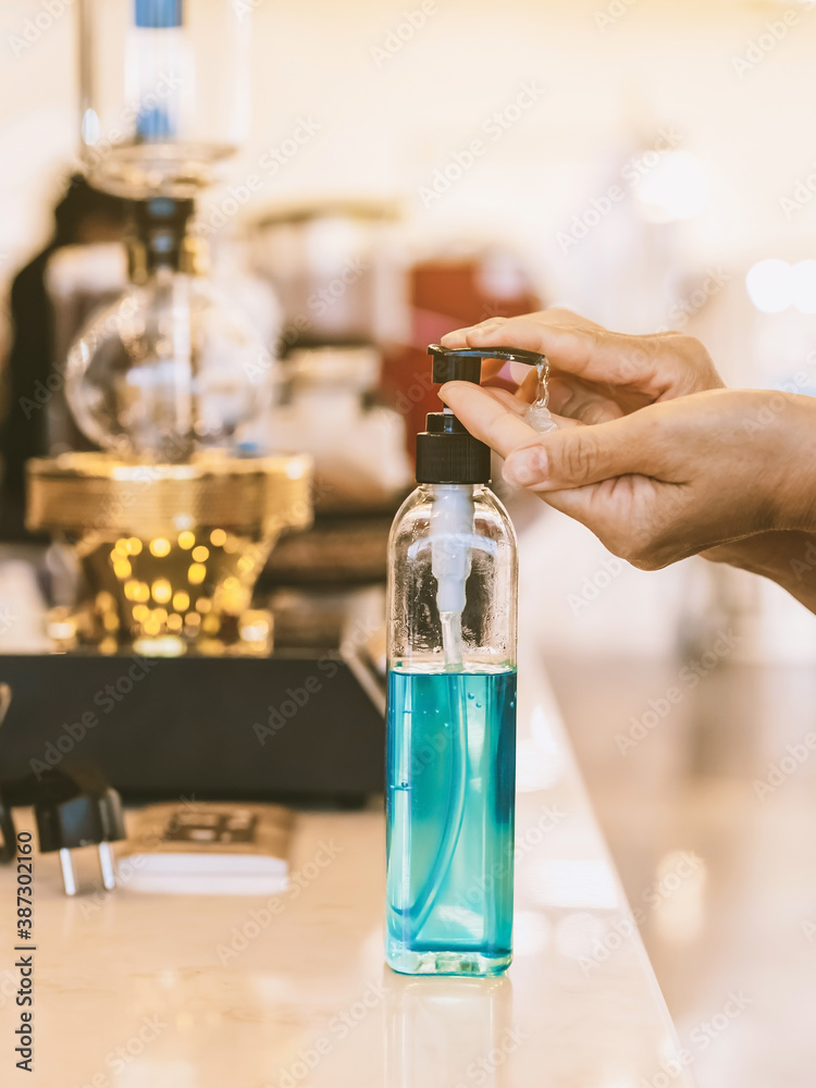 Hands of woman pressed blue alcohol gel bottle to prevent the spreading of the Coronavirus (Covid-19) before entrance to coffee shop. New normal lifestyle. Selective focus on alcohol gel bottle. Hands of woman pressed blue alcohol gel bottle to prevent the spreading of the Coronavirus (Covid-19) before entrance to coffee shop. New normal lifestyle. Selective focus on alcohol gel bottle.