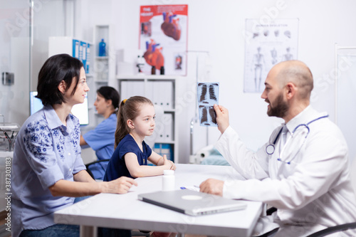 Pediatrician explaining diagnosis to mother and child holding radiography in hospital office. Healthcare physician specialist in medicine providing health care services treatment examination.