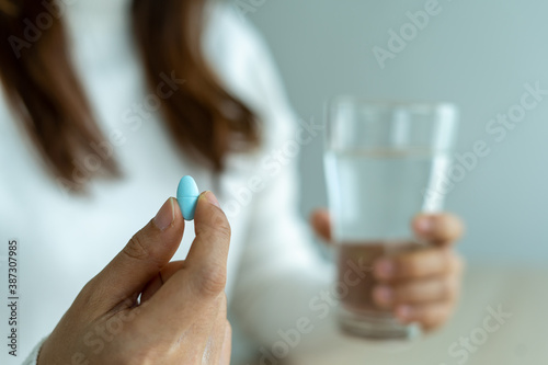 The woman's hand holds a pill and a glass of water. The patient is about to take the medicine. Taking care of the sick body using antibiotics.