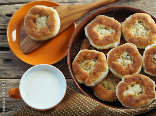 Country style. Freshly baked homemade belyashi, in a plate on a wooden background with a wooden kitchen spatula and a cup of milk. Healthy natural food.