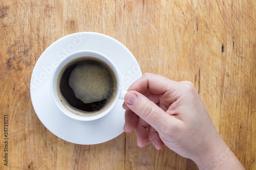 Hand holding cup of coffee with wooden background