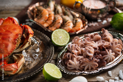 Plates with assorted seafood. Cooked crab, baby octopuses and tiger shrimps served with ice cubes, lime and seashells on rustic wooden background. Seafood concept. Delicious for gourmet.