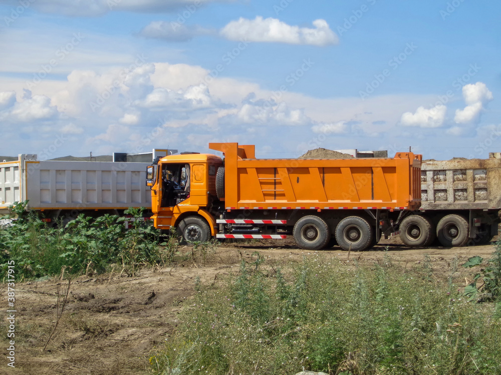 Trucks on the construction site. Road construction. Bright trucks. Summer landscape. Blue sky. Ust-Kamenogorsk (Kazakhstan)