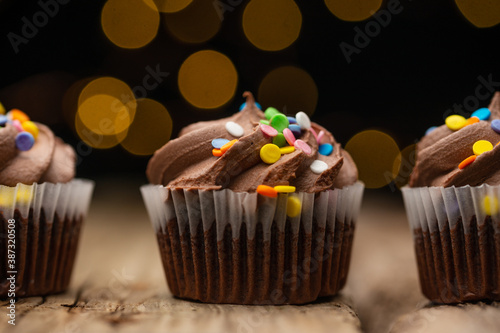 Close-up view of tasty chocolate cupcake on rustic wooden table with yellow lights on black background. Sweet dessert. Bakery concept. Delicious food.