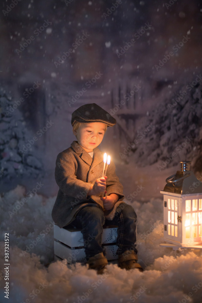 Little boy, looking at flame from match, sitting in the snow Little boy, looking at flame from match, sitting in the snow