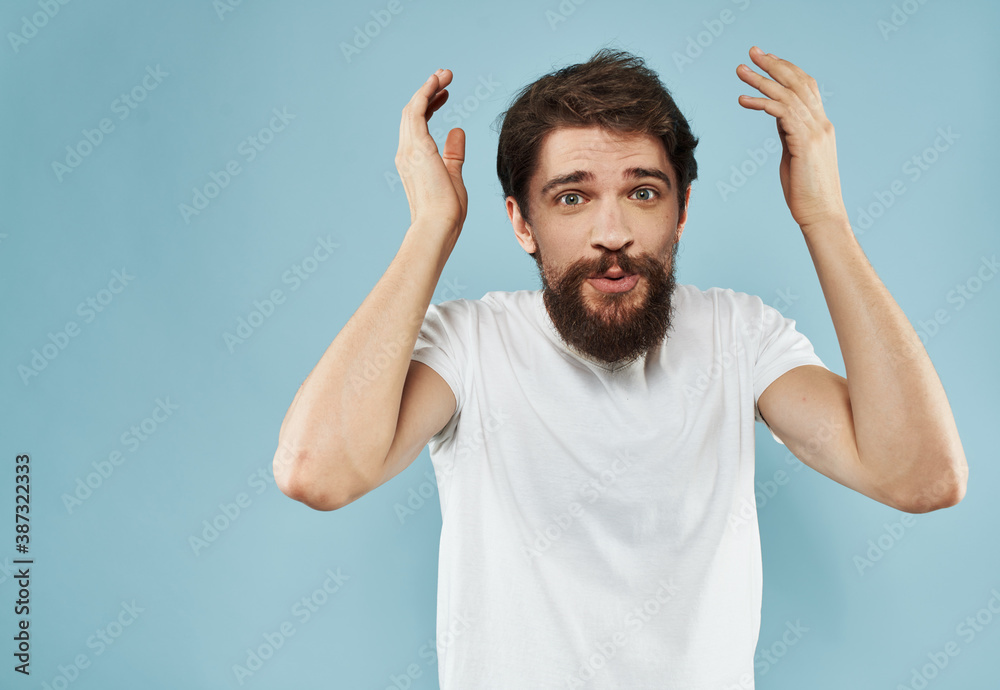 An energetic man gesturing with his hands on a blue background and a thick beard in a white t-shirt