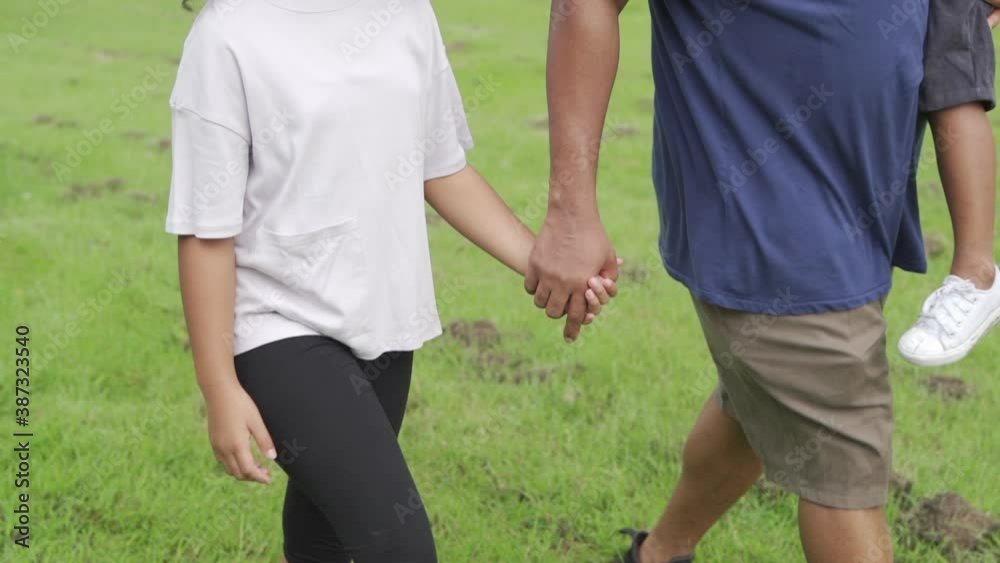 Happy affectionate mixed race family. African father carrying and holding hands his two little daughter walking in the park. Dad and cute child girl spending time together in outdoor weekend vacation. Happy affectionate mixed race family. African father carrying and holding hands his two little daughter walking in the park. Dad and cute child girl spending time together in outdoor weekend vacation.