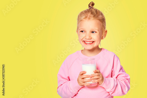 Cute little girl holding a large glass of milk. Kid 4-5 year old posing in studio on yellow background
