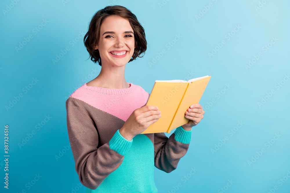 Photo portrait of cheerful happy female student holding yellow book smiling isolated on bright blue color background Photo portrait of cheerful happy female student holding yellow book smiling isolated on bright blue color background