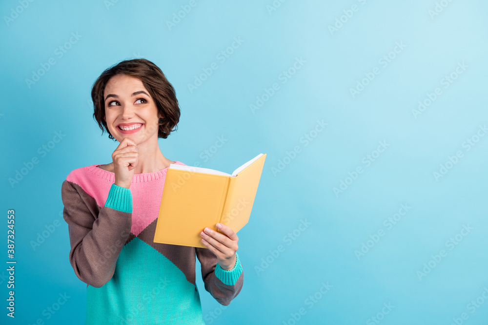 Photo portrait of smiling dreamy girl looking up at blank space smiling holding book touching face isolated on vivid blue color background Photo portrait of smiling dreamy girl looking up at blank space smiling holding book touching face isolated on vivid blue color background