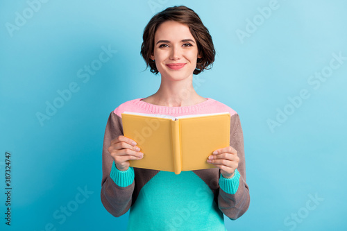 Photo portrait of cute female girl with short hair keeping yellow book smiling isolated on bright blue color background