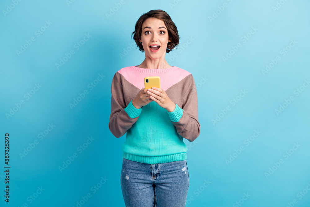 Photo portrait of excited surprised woman holding phone in two hands isolated on pastel light blue colored background Photo portrait of excited surprised woman holding phone in two hands isolated on pastel light blue colored background