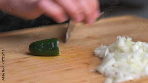 Left handed man slicing and dicing a fresh green jalapeno pepper into cubes on wooden cutting board photo