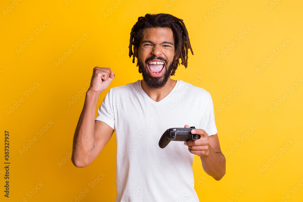 Photo of mad black guy hold joystick joystick open mouth raise arm fist wear white t-shirt isolated yellow color background Photo of mad black guy hold joystick joystick open mouth raise arm fist wear white t-shirt isolated yellow color background