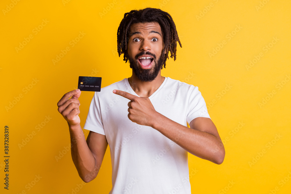 Photo of black stylish guy dreadlocks direct forefinger hold credit card open mouth wear white t-shirt isolated yellow color background Photo of black stylish guy dreadlocks direct forefinger hold credit card open mouth wear white t-shirt isolated yellow color background