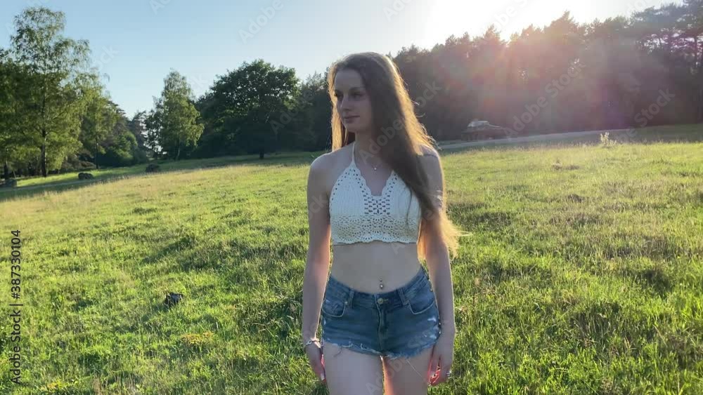 Hübsche junge Frau spaziert über eine Wiese im Park an einem warmen sonnigen Abend im Sommer
