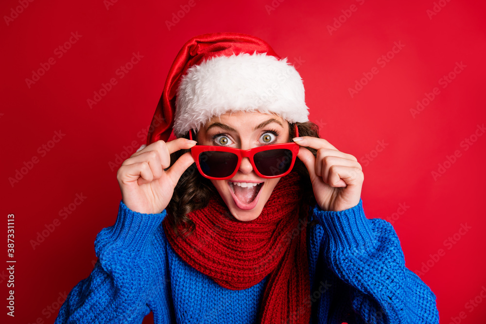 Photo portrait of cute surprised girl taking off holding glasses with fingers open mouth wearing blue pullover scarf santa hat isolated on vivid red colored background Photo portrait of cute surprised girl taking off holding glasses with fingers open mouth wearing blue pullover scarf santa hat isolated on vivid red colored background