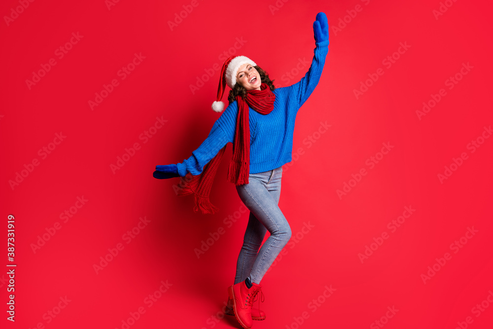 Photo portrait of jolly girl dancing fooling around cheering posing extending hands arms laughing wearing blue pullover scarf santa hat isolated on bright red colored background
