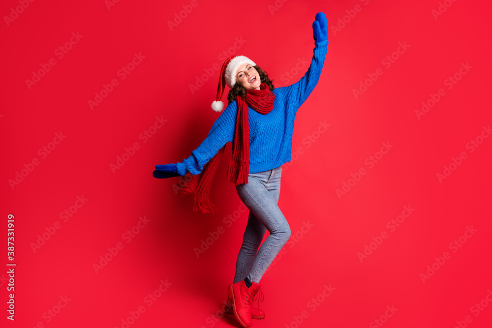 Photo portrait of jolly girl dancing fooling around cheering posing extending hands arms laughing wearing blue pullover scarf santa hat isolated on bright red colored background Photo portrait of jolly girl dancing fooling around cheering posing extending hands arms laughing wearing blue pullover scarf santa hat isolated on bright red colored background