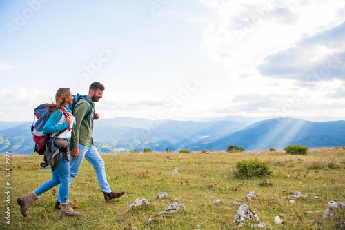 Young couple enjoying their in the mountains on backpacking trip. Side view with big beautiful mountains on the background.