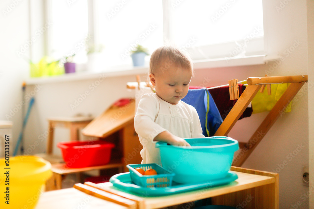 Toddler child plays with water in a basin, developing sensory activities with water and objects, montessori and earlier child development, toddler independence Toddler child plays with water in a basin, developing sensory activities with water and objects, montessori and earlier child development, toddler independence