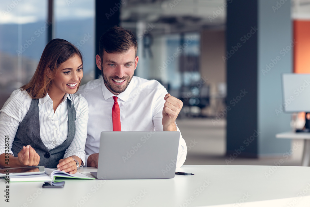 Coworkers celebrating success in modern office using laptop computer Coworkers celebrating success in modern office using laptop computer