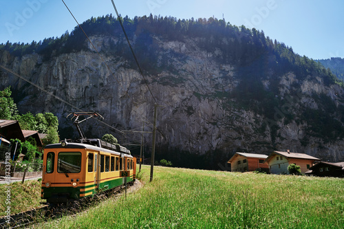 Beautiful mountains landscape. Yellow-green train running through the Swiss Grindelwald Village, Switzerland.