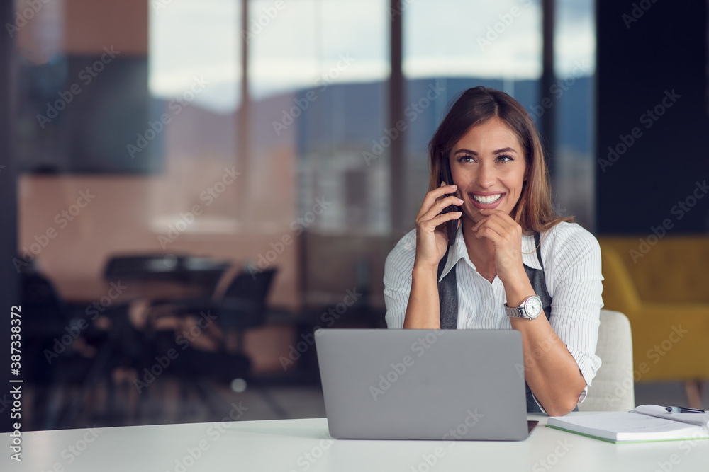 A young woman with computer and smartphone indoors, working in office. A young woman with computer and smartphone indoors, working in office.