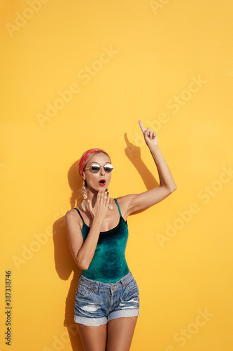 Your text here. I have an idea!Amazed beautiful young woman pointing up while standing against yellow wall.