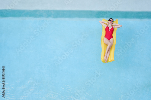Enjoying suntan. Tropical vacation concept. Top view of young woman on the yellow air mattress in the swimming pool. © luengo_ua