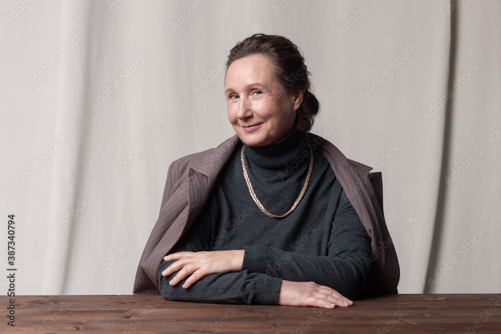 Good-looking and stylish caucasian elderly businesswoman sitting at the table and smiling. 