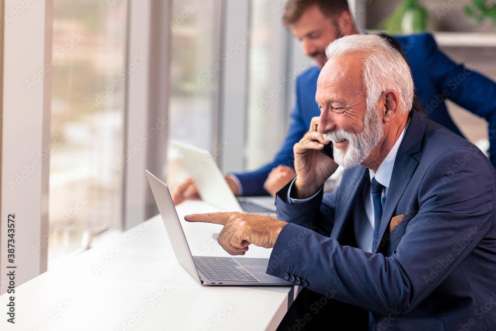 Senior manager using a mobile phone with young colegues in background