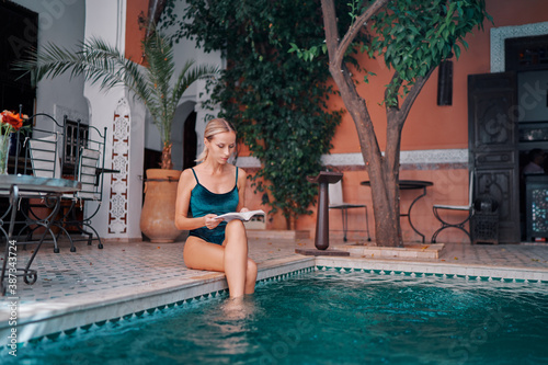 Retreat and vacation. Beautiful young woman reading book in spa swimming pool in beautiful moroccan backyard. © luengo_ua