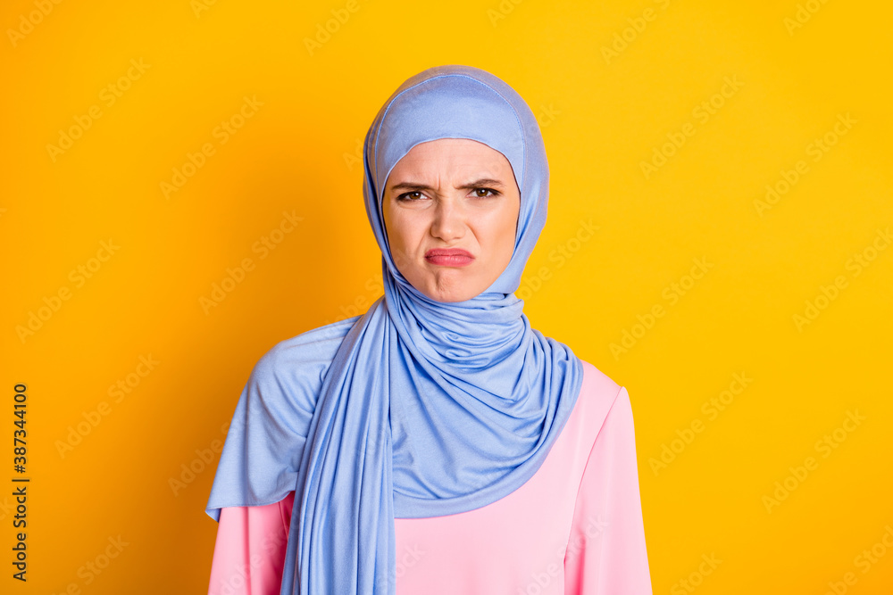 Close-up portrait of attractive displeased capricious muslimah wearing hijab pursue lips isolated on bright yellow color background Close-up portrait of attractive displeased capricious muslimah wearing hijab pursue lips isolated on bright yellow color background