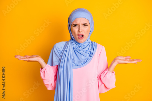 Portrait of pretty desperate muslimah wearing hijab indifferent misunderstanding expression isolated on bright yellow color background photo